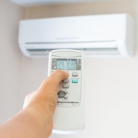 A person is operating the remote control of an air conditioner.