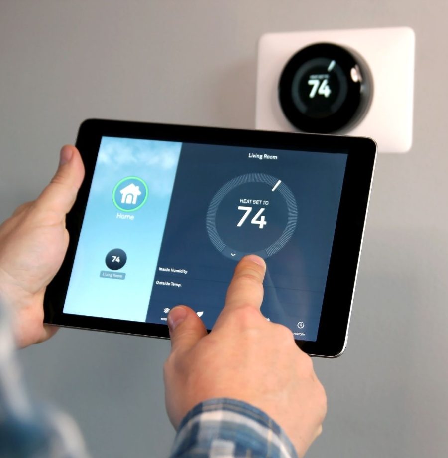 A person is holding an ipad in front of the thermostat.